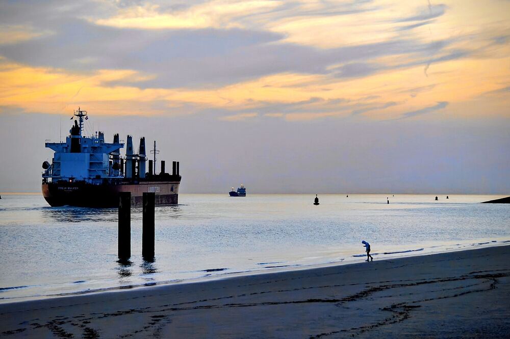 Een vrachtschip vaart bij zonsondergang over de Westerschelde langs het strand van Vlissingen